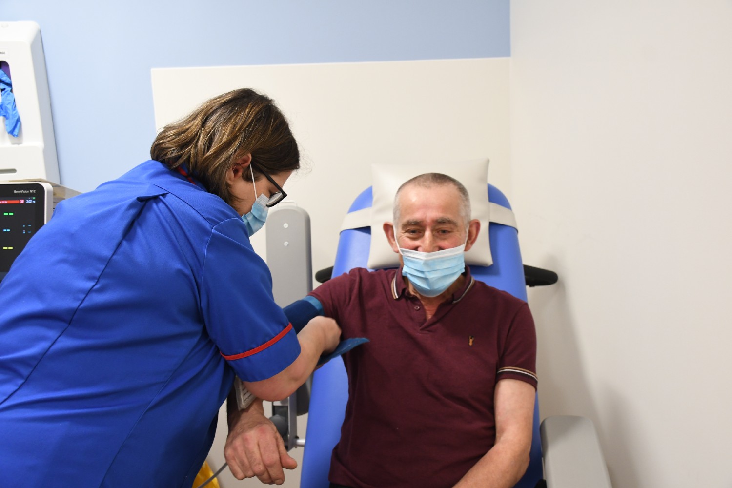 A person in a blue uniform attends to a person in a burgandy t-shirt with their arm outstretched.