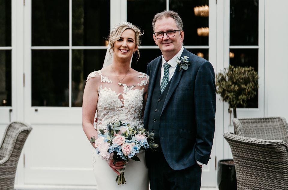 Heart transplant recipient Alan in a smart suit, standing next to his daughter Megan on her wedding day. She is wearing a white wedding dress.