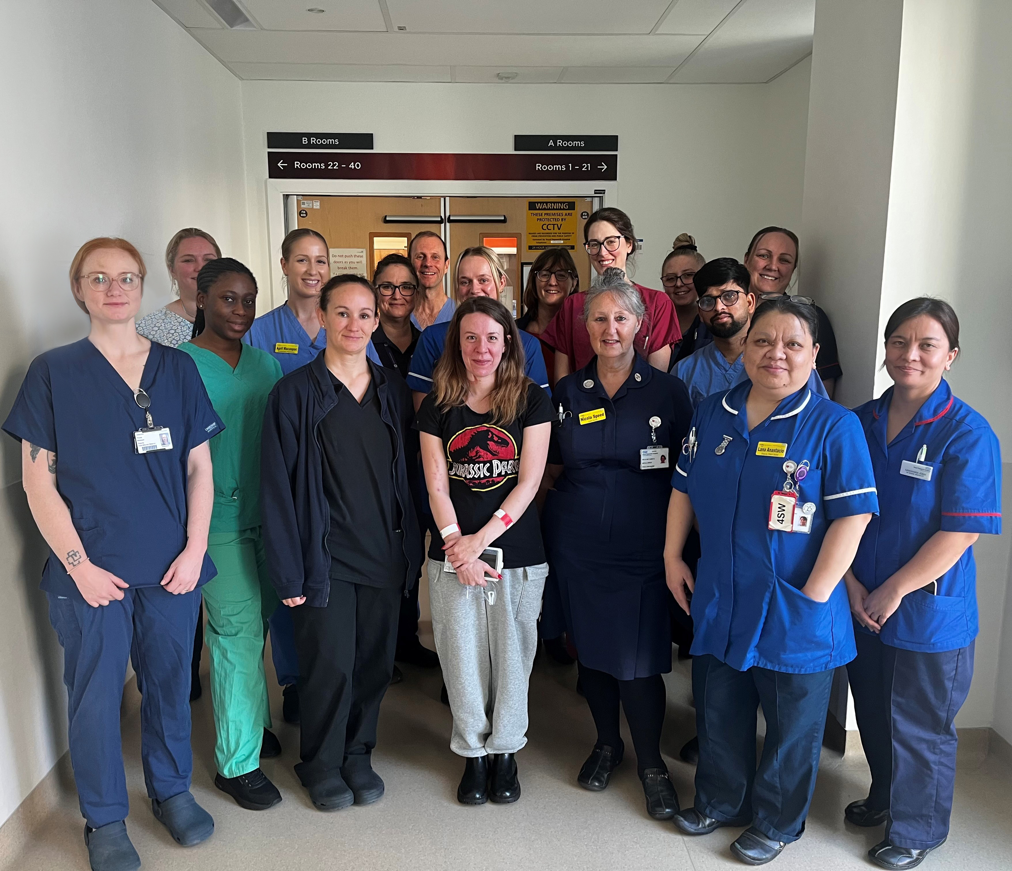 Photo of healthcare professionals smiling and wearing scrubs and nurses' uniforms gathered around a young lady who is also smiling.