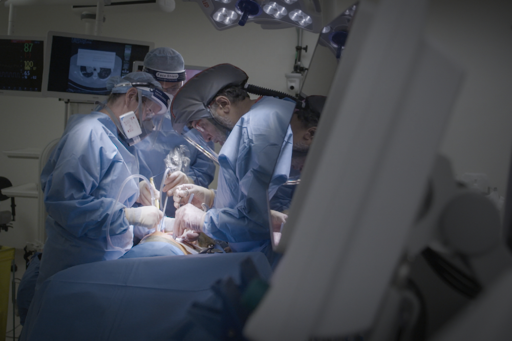 People in blue gowns and masks operating. 