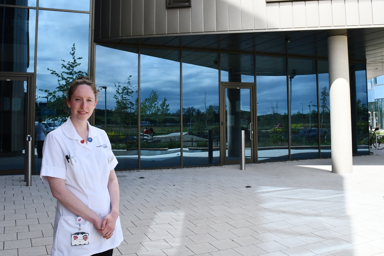 A person in a white top standing outside in front of a building with glass panels.