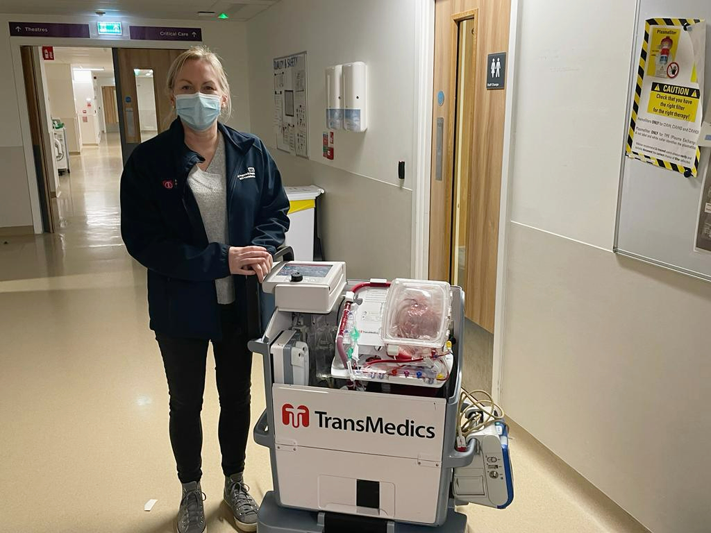 A person standing in a corridor next to a machine containing a heart in a case.