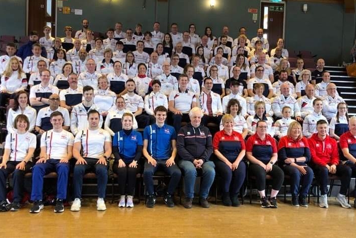 A group shot of dozens of people sat in rows for a team photo