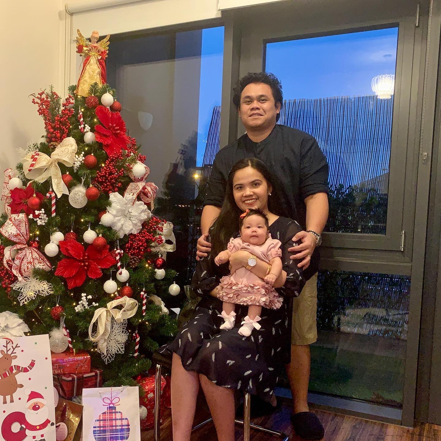 A man, woman and baby beside a Christmas tree