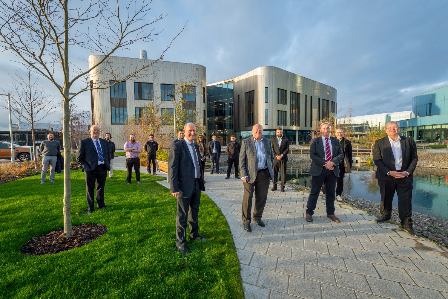 People standing outside a building, with a pond on the right of the image.