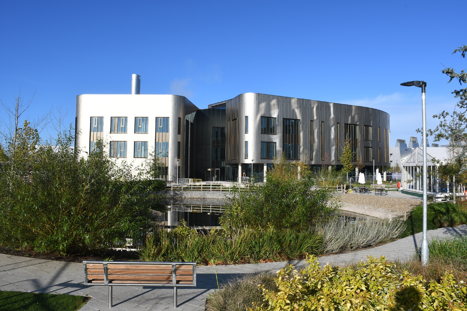 A building with bronze cladding and glass windows, blue skies and a pond in the foreground.