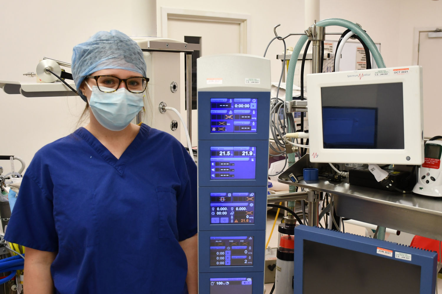 A woman in scrubs stands next to a machine.