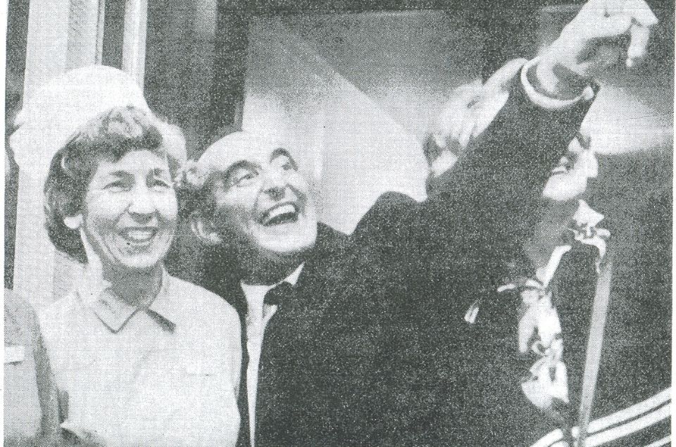 Keith Castle standing on a balcony, smiling and pointing. A black and white photo.jpg