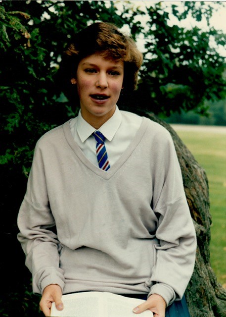 Katie, with blue lips, mouth and cheeks, in a grey school jumper.