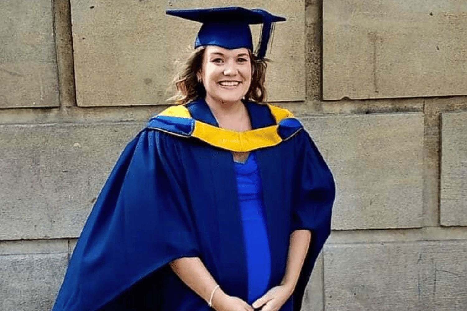 Jade in a blue dress, navy blue graduation gown with a gold collar and blue mortar board hat.