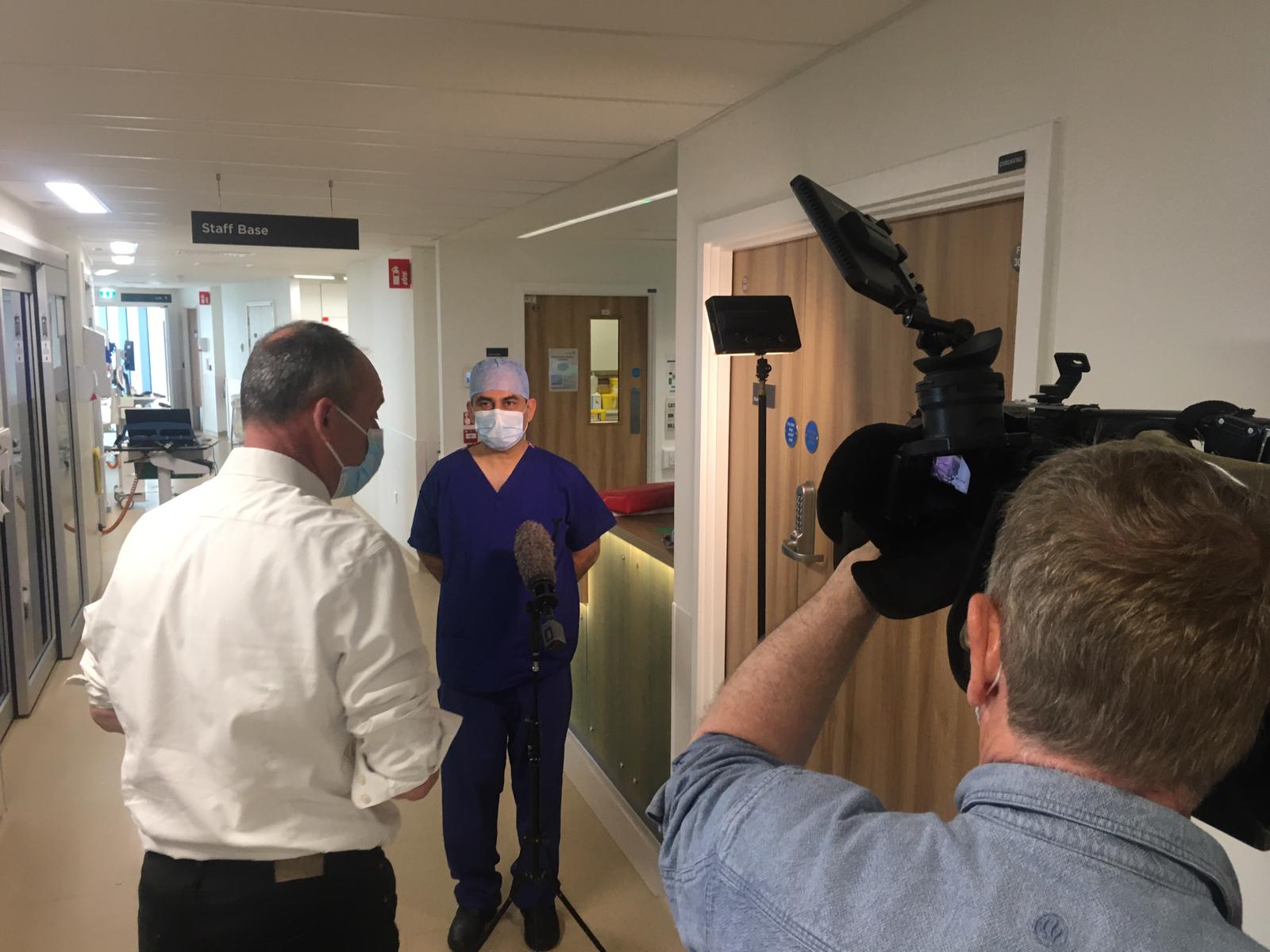 A surgeon being interviewed by a TV reporter, with a person holding a camera. 