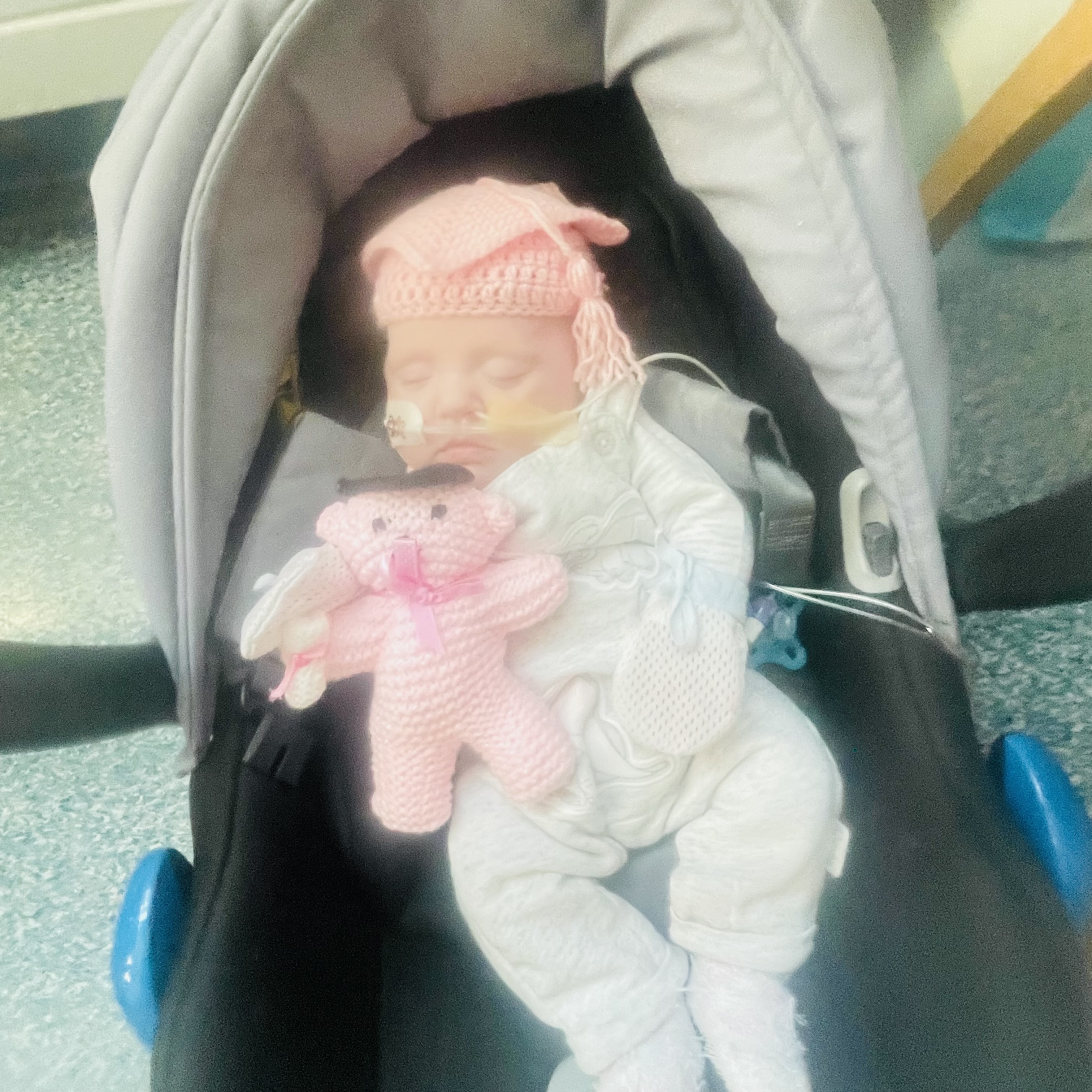 Photo of a tiny baby fast asleep in a car seat, with a tube in its nose. 