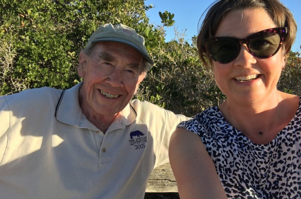 Sir Terence with daughter Mary sitting in the sunshine, smiling, with green bushes behind them.jpg