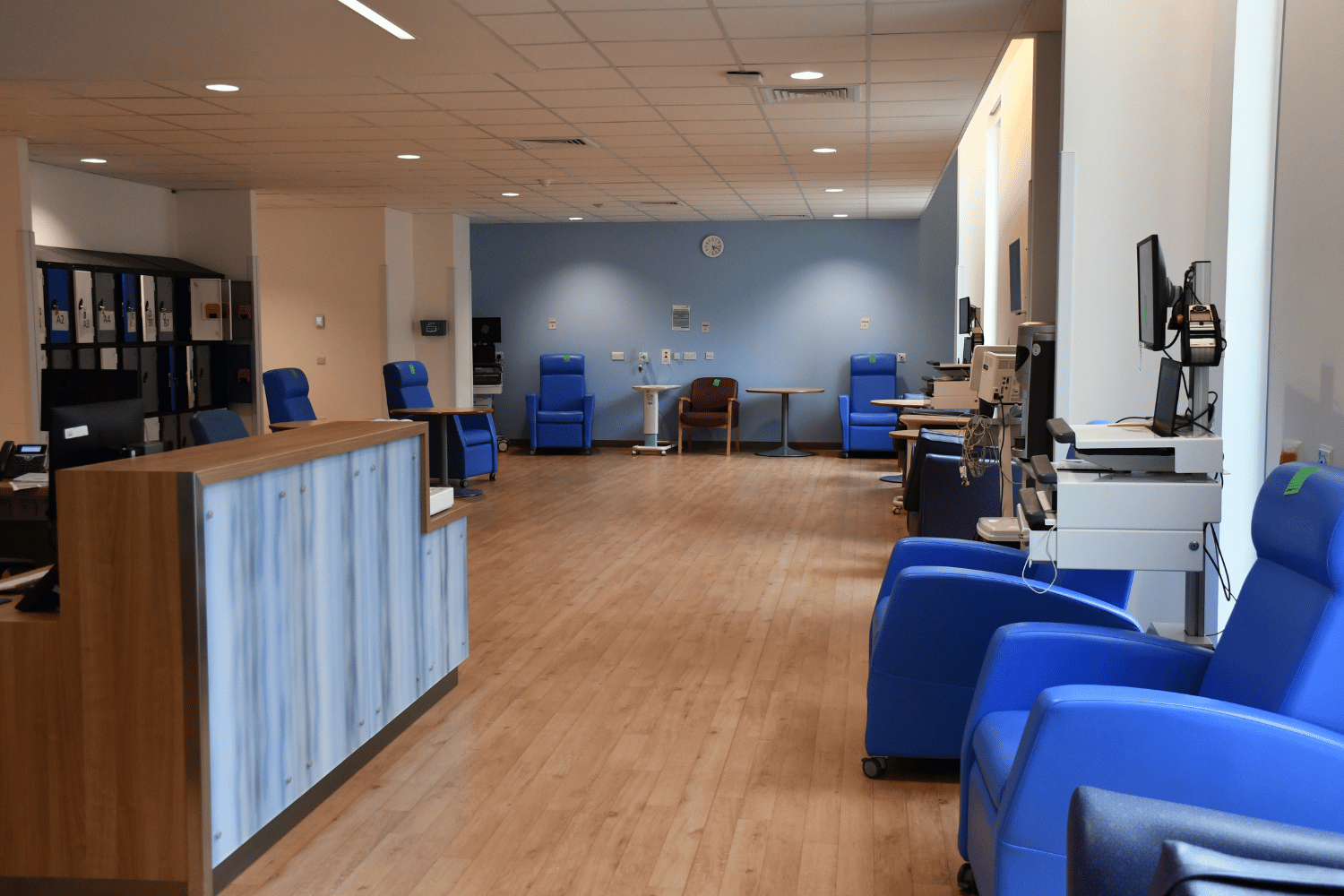 A large hospital lounge with reclining chairs and a nursing station.